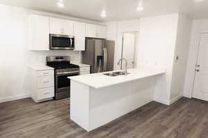 Kitchen with sink, stainless steel appliances, dark hardwood / wood-style flooring, kitchen peninsula, and white cabinets