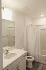 Full bathroom with wood-type flooring, vanity, shower / tub combo, and toilet