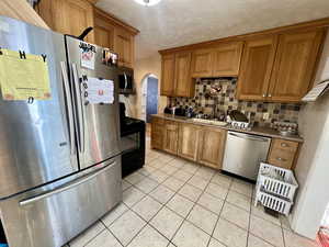 Kitchen with light tile patterned floors, stainless steel appliances, backsplash, a textured ceiling, and sink