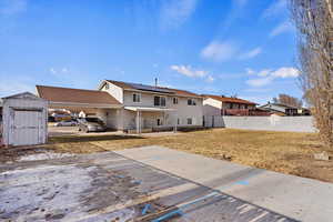 Back of property featuring solar panels, a shed, a carport, and a lawn