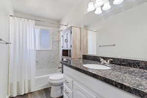 Full bathroom with hardwood / wood-style floors, vanity, toilet, and shower / bath combo with shower curtain