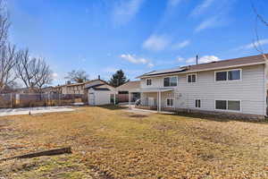 Rear view of house featuring solar panels, a patio area, and a storage shed