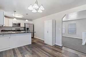 Kitchen featuring dark hardwood / wood-style floors, white cabinetry, stainless steel appliances, and decorative light fixtures