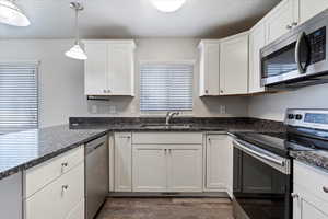 Kitchen featuring dark stone counters, stainless steel appliances, sink, white cabinets, and hanging light fixtures