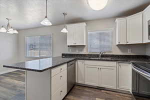 Kitchen with kitchen peninsula, white cabinetry, sink, and pendant lighting