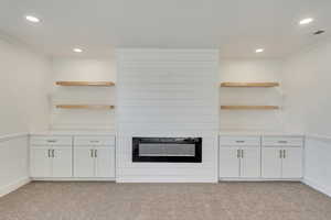 Kitchen with crown molding, white cabinets, light carpet, and a large fireplace