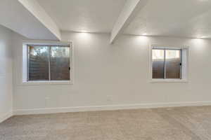 Carpeted spare room featuring a wealth of natural light, a textured ceiling, and beamed ceiling