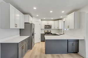 Kitchen with kitchen peninsula, gray cabinetry, stainless steel appliances, sink, and light hardwood / wood-style floors