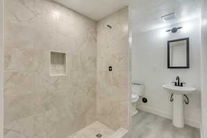 Bathroom featuring toilet, a textured ceiling, tiled shower, and hardwood / wood-style flooring