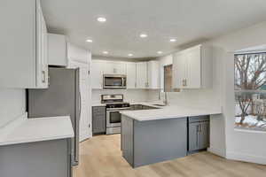 Kitchen featuring gray cabinetry, white cabinets, sink, light wood-type flooring, and appliances with stainless steel finishes