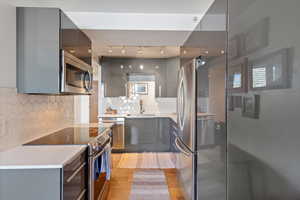 Kitchen with tasteful backsplash, gray cabinetry, stainless steel appliances, sink, and light hardwood / wood-style flooring