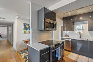 Kitchen featuring decorative backsplash, sink, stainless steel appliances, and light hardwood / wood-style floors