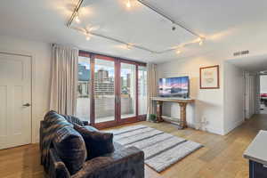 Living room with light hardwood / wood-style floors, rail lighting, and french doors