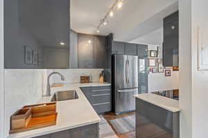 Kitchen featuring stainless steel fridge, light wood-type flooring, backsplash, sink, and gray cabinets