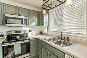 Kitchen with hanging light fixtures, stainless steel appliances, and green cabinetry