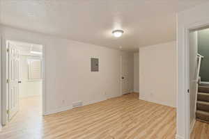 Empty room featuring electric panel, light hardwood / wood-style floors, and a textured ceiling