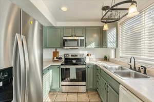 Kitchen with sink, pendant lighting, green cabinetry, and appliances with stainless steel finishes