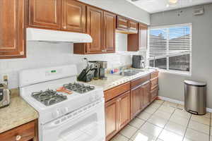 Kitchen featuring backsplash, sink, ceiling fan, white gas range, and light tile patterned flooring