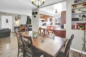 Dining space with ceiling fan with notable chandelier, a textured ceiling, and light hardwood / wood-style floors