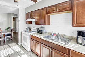 Kitchen featuring decorative backsplash, white range with gas stovetop, sink, and light tile patterned floors