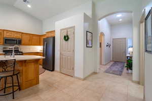 Kitchen featuring high vaulted ceiling, light tile patterned flooring, a breakfast bar area, and appliances with stainless steel finishes