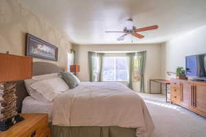 Primary bedroom with ceiling fan, light carpet and bay window