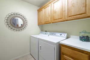 Clothes washing area with cabinets, light tile patterned floors, and washing machine and dryer