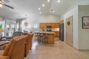 Kitchen with a center island with sink, a kitchen breakfast bar, appliances with stainless steel finishes, decorative light fixtures, and light tile flooring