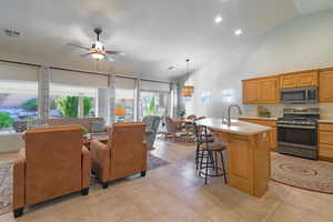 Great room featuring tile floors, ceiling fan, sink, stainless steel appliances, an island with sink, and pendant lighting