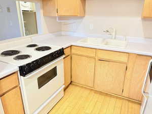 Kitchen featuring white range with electric stovetop, light brown cabinets, sink, and light hardwood / wood-style flooring