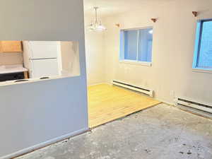 Kitchen featuring white refrigerator, hanging light fixtures, a baseboard radiator, a notable chandelier, and wood-type flooring