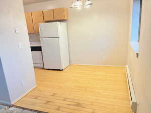 Kitchen featuring an inviting chandelier, light hardwood / wood-style flooring, a baseboard heating unit, decorative light fixtures, and white appliances