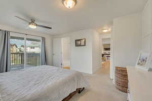 Primary bedroom with access to exterior, ensuite bathroom, light colored carpet, and ceiling fan