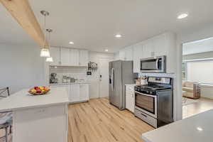 Kitchen featuring appliances with stainless steel finishes, light wood-type flooring, white cabinetry, and hanging light fixtures