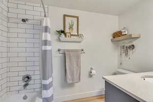 Full bathroom attached to primary suite, featuring hardwood / wood-style floors, vanity, toilet, and shower / tub combo with curtain