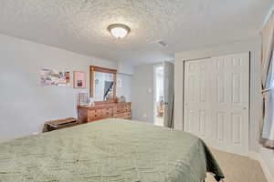 Bedroom featuring a textured ceiling, light colored carpet, and a closet