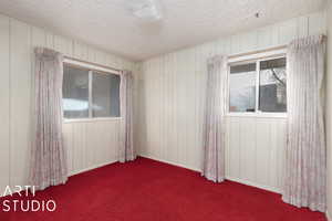 Carpeted empty room with a textured ceiling and wooden walls