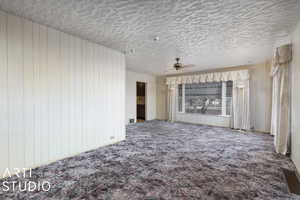 Unfurnished living room featuring ceiling fan, carpet floors, and a textured ceiling