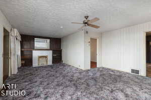 Unfurnished living room with carpet, a textured ceiling, ceiling fan, wooden walls, and a fireplace