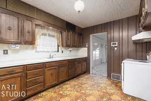 Kitchen featuring light carpet, a textured ceiling, sink, washer / clothes dryer, and wood walls