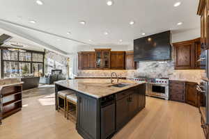 Kitchen with light stone countertops, custom range hood, sink, premium stove, and an island with sink