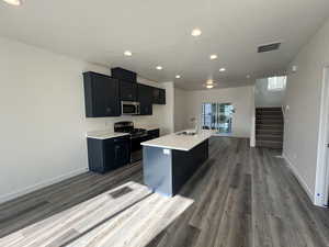 Kitchen with dark hardwood / wood-style flooring, a textured ceiling, stainless steel appliances, a kitchen island with sink, and sink