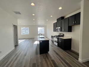 Kitchen with a center island with sink, sink, dark hardwood / wood-style floors, a textured ceiling, and stainless steel appliances