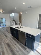 Kitchen with stainless steel dishwasher, a kitchen island with sink, sink, blue cabinetry, and light hardwood / wood-style flooring