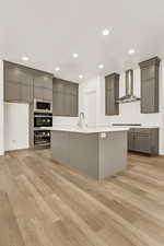 Kitchen with gray cabinets, built in microwave, light hardwood / wood-style floors, and wall chimney range hood