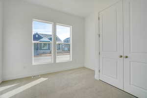 Unfurnished bedroom with light colored carpet and baseboards