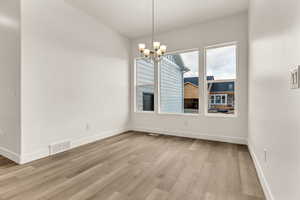 Unfurnished dining area featuring an inviting chandelier and light wood-type flooring