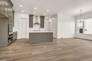 Kitchen featuring wall chimney exhaust hood, hanging light fixtures, a chandelier, and light hardwood / wood-style flooring