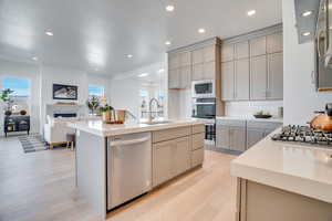 Kitchen with gray cabinetry, appliances with stainless steel finishes, open floor plan, light wood finished floors, and an island with sink