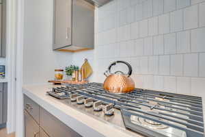 Kitchen view of gray cabinets, stainless steel gas stovetop, light countertops, and tasteful backsplash